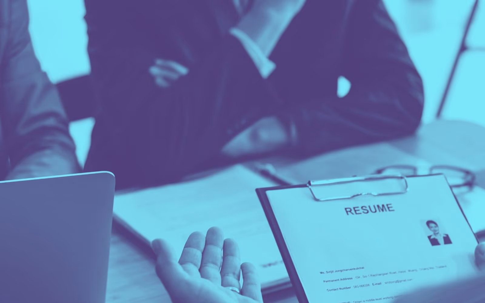 A résumé on a clipboard held across a desk during an interview, in a blue duotone treatment.